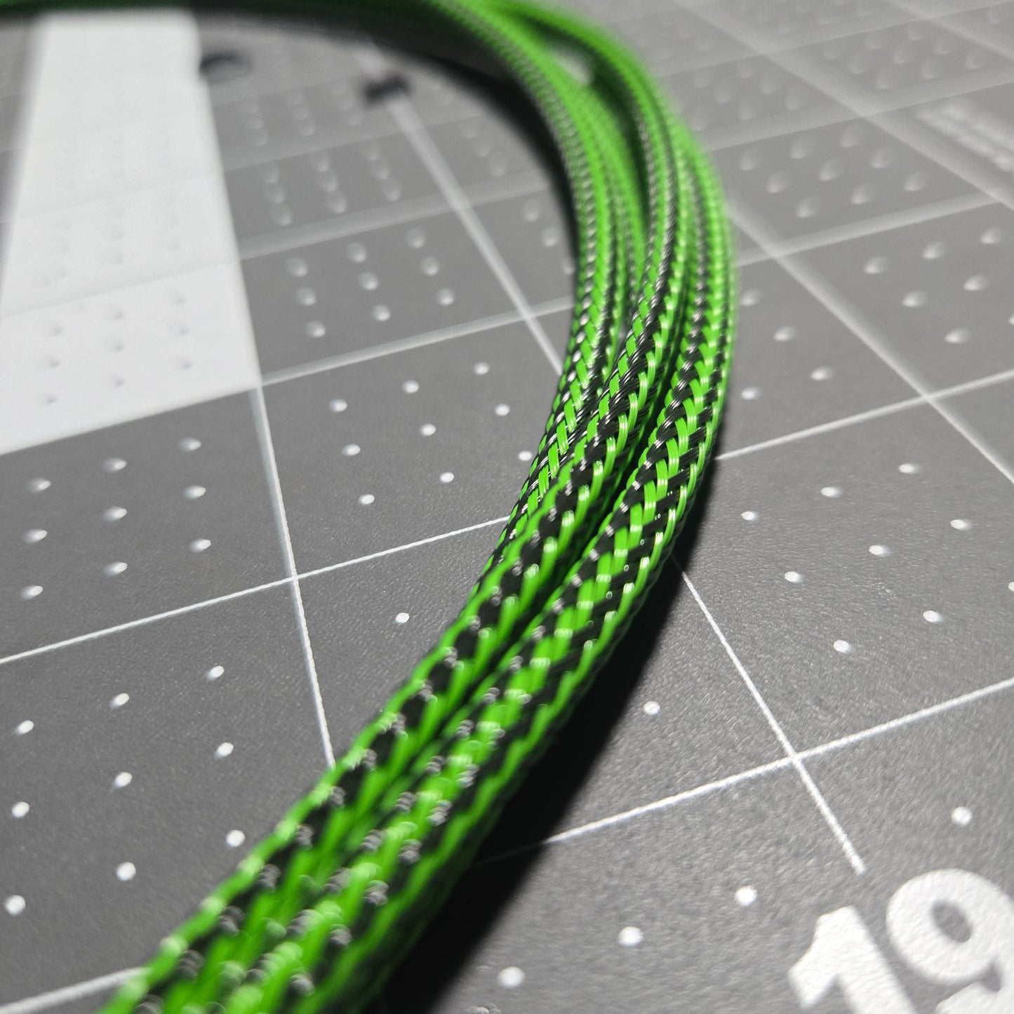 Close-up of green braided cable on a gray cutting mat with grid lines.